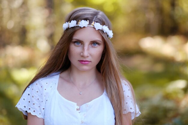 Sommersprossige Frau mit Blumenkranz auf ihrem Kopfporträt im Herbstwald bei Tageslicht.