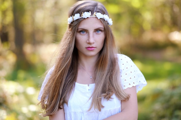 Sommersprossige Frau mit Blumenkranz auf ihrem Kopfporträt im Herbstwald bei Tageslicht.