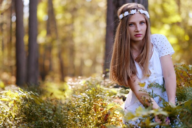 Sommersprossige Frau mit Blumenkranz auf ihrem Kopfporträt im Herbstwald bei Tageslicht.