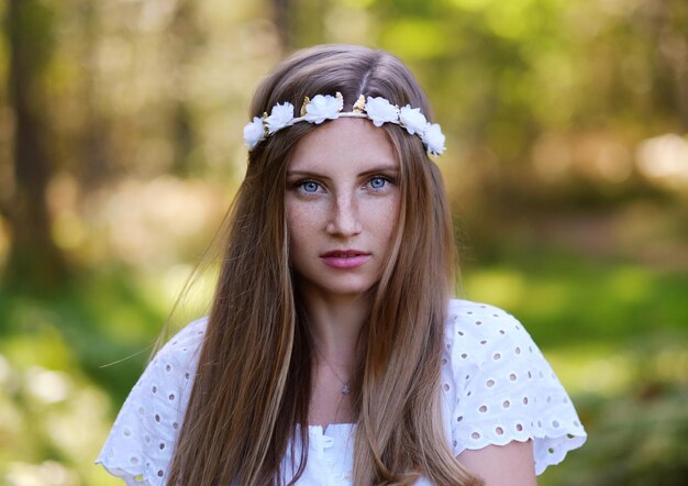 Sommersprossige Frau mit Blumenkranz auf ihrem Kopfporträt im Herbstwald bei Tageslicht.