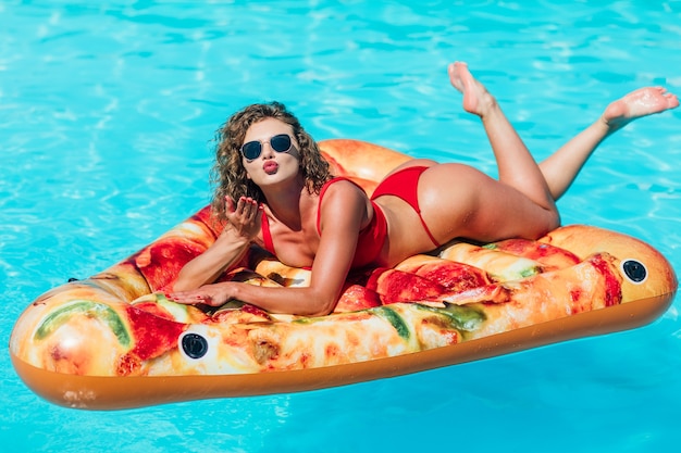 Sommerurlaub. Genießen der Sonnenbräune Frau im Bikini auf der aufblasbaren Matratzenpizza im Schwimmbad. Vorbildliches Mädchen.