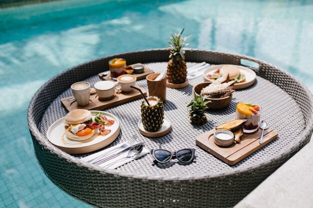 Sonnenbrille, Burger und Saft. Tisch mit exotischem Mittagessen im Schwimmbad.