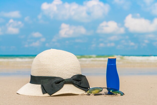 Sonnenbrille, Sonnencreme und Hut auf weißem Sandstrand