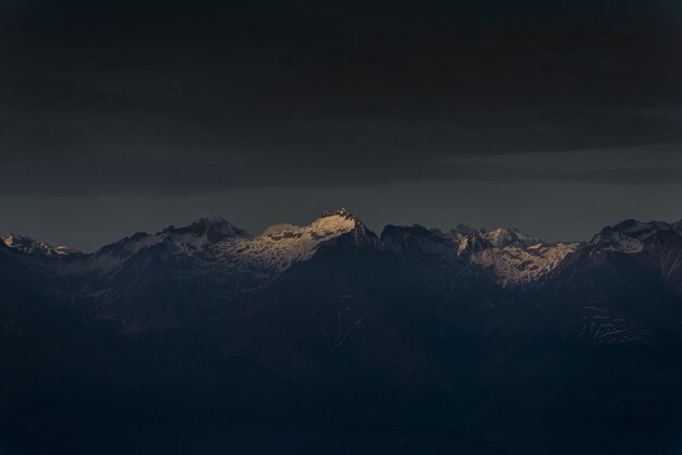 Sonnenlicht, das einen einzelnen Berggipfel bei Sonnenuntergang mit dunklem bewölktem Himmel scheint