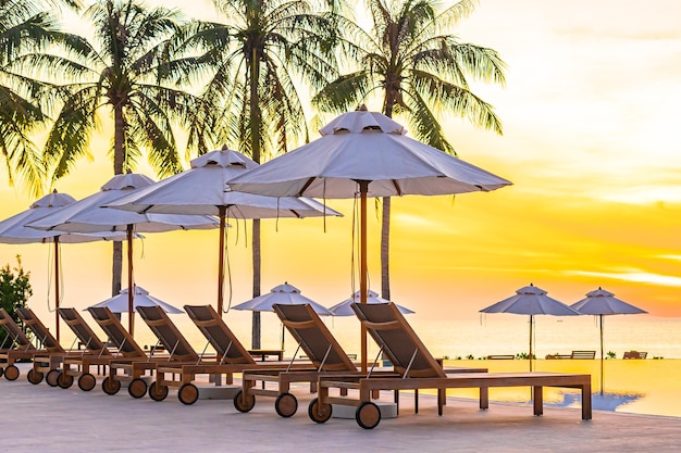 Sonnenschirm Liegestuhl um Pool im Hotel Resort mit Meer Ozean Strand und Kokospalme bei Sonnenuntergang oder Sonnenaufgang Zeit