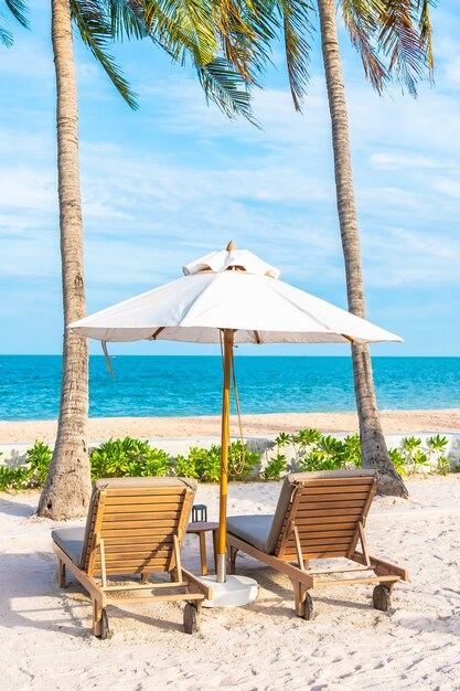 Sonnenschirm und Liegestuhl um Außenpool im Hotelresort mit Meeresmeerstrand und Kokospalme