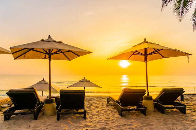 Sonnenschirm und Stuhl am schönen Strand und Meer zur Sonnenaufgangzeit für Reisen und Urlaub