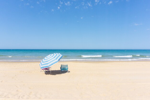 Sonnenschirm und zwei Liegestühle am Strand