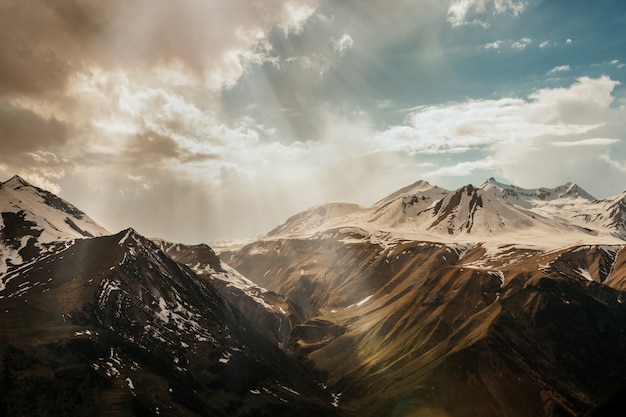 Sonnenstrahlen dringen durch die Wolken in das verschneite Hochgebirge