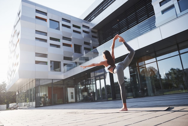 Sonniger Sommermorgen. Junge athletische Frau, die Handstand auf Stadtparkstraße unter modernen städtischen Gebäuden tut. Übung im Freien gesunden Lebensstil