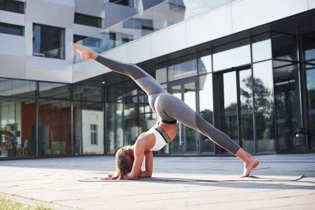 Sonniger Sommermorgen. Junge athletische Frau, die Handstand auf Stadtparkstraße unter modernen städtischen Gebäuden tut. Übung im Freien gesunden Lebensstil