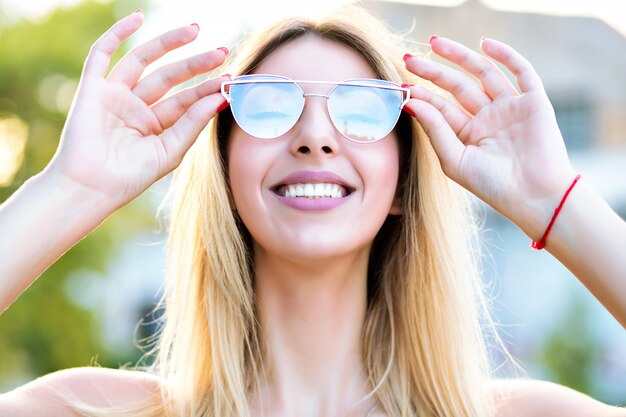 Sonniges Frühlingssommerporträt der glücklichen blonden Frau genießen schönen warmen Tag lächelnd und schließen ihre Augen, tragen stilvolle trendige Brille, positive Stimmung.