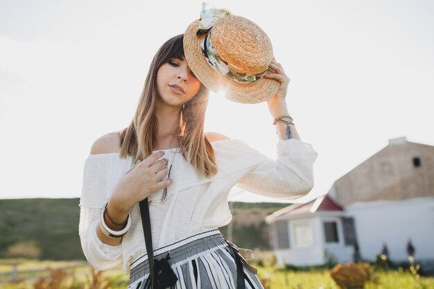 Sonniges Porträt der lächelnden jungen schönen stilvollen Frau, Frühlingssommer-Modetrend, Boho-Art, Strohhut, Landschaftswochenende, sonniger, schwarzer Geldbeutel