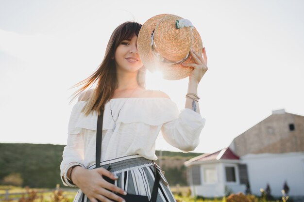 Sonniges Porträt der lächelnden jungen schönen stilvollen Frau, Frühlingssommer-Modetrend, Boho-Art, Strohhut, Landschaftswochenende, sonniger, schwarzer Geldbeutel