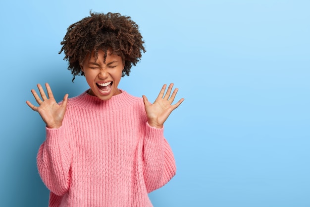 Kostenloses Foto sorglose freudige frau mit einem afro, der in einem rosa pullover aufwirft