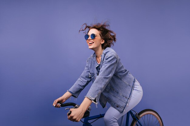 Sorglose junge Dame mit trendiger Brille, die auf dem Fahrrad fährt Erstaunliches lustiges Mädchen, das auf dem Fahrrad sitzt und lächelt