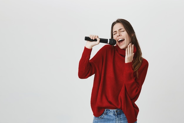 Sorglose süße Frau, die Karaoke im Mikrofon singt