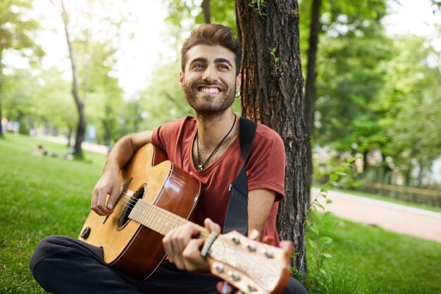 Sorgloser hübscher Kerl, der Gitarre im Park spielt
