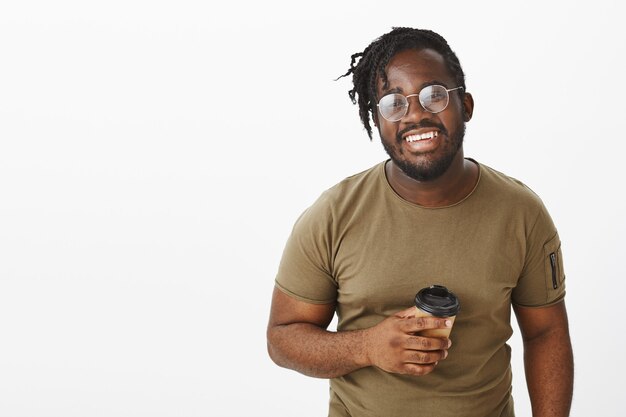 sorgloser Typ mit Brille posiert mit seinem Kaffee an der weißen Wand