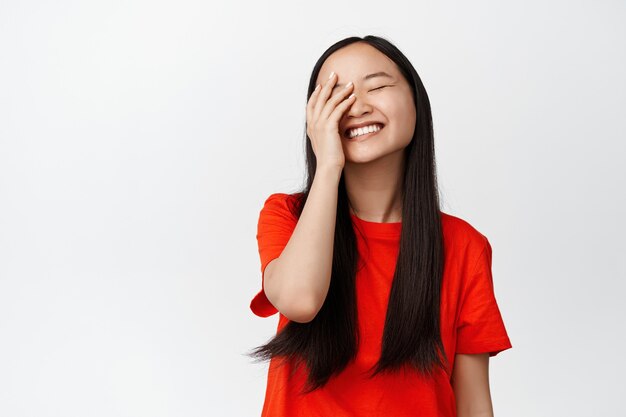 Sorgloses asiatisches Mädchen, das lacht und lächelt, Augen schließen und glücklich auf Weiß stehen. Platz kopieren