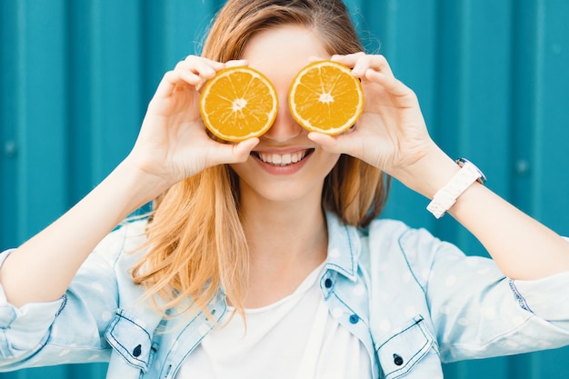 Sorgloses junges schönes Mädchen, das zwei halfs auf Orangen anstelle der Gläser über ihren Augen verwendet