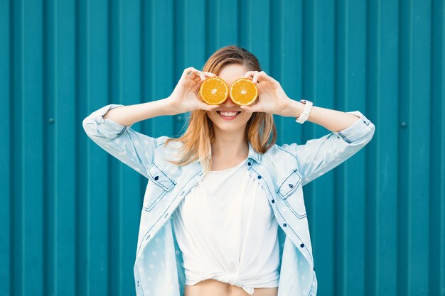 Sorgloses junges schönes Mädchen, das zwei halfs auf Orangen anstelle der Gläser über ihren Augen verwendet