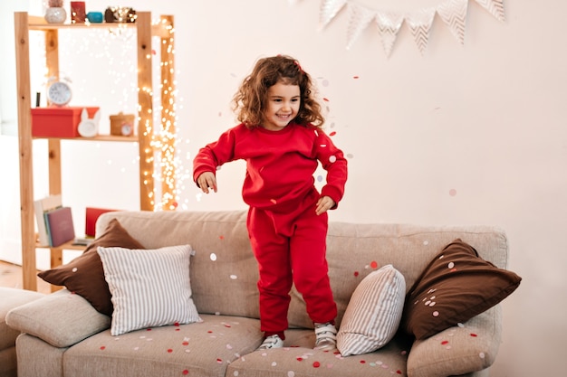 Sorgloses Kind im Pyjama, das auf Sofa springt. Brünettes kleines Mädchen, das auf Couch steht.