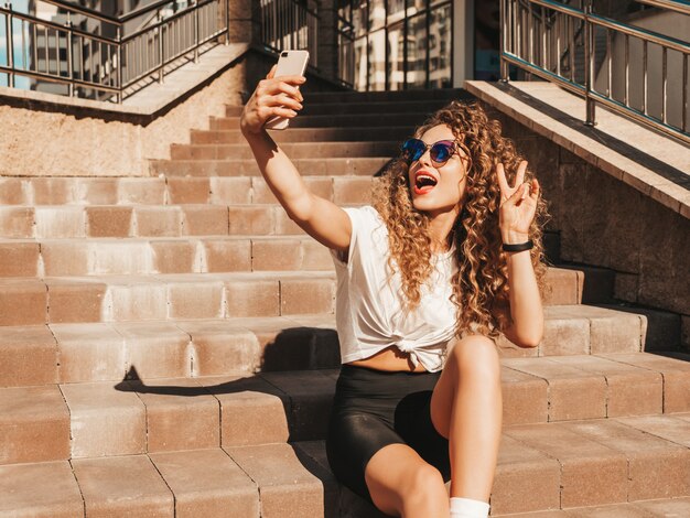 Sorgloses Mädchen, das auf der Treppe in der Straße sitzt und ein Selfie macht
