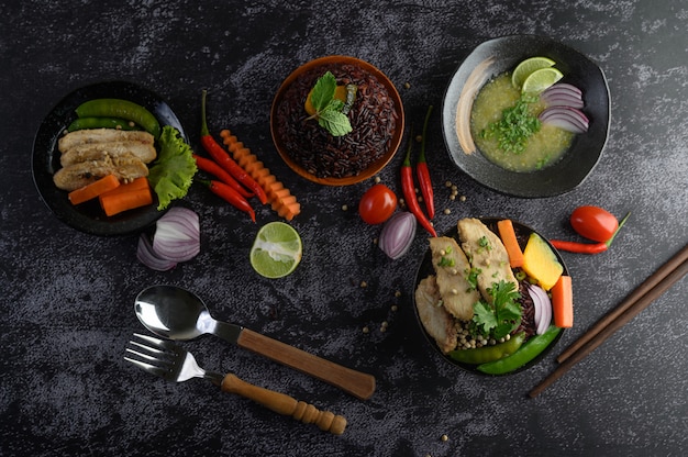 Sortierte Nahrung und Teller des Gemüses, des Fleisches und der Fische auf einer schwarzen Steintabelle. Ansicht von oben.