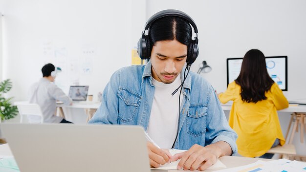 Soziale Distanzierung des Geschäftsmanns in Asien in einer neuen normalen Situation zur Virenprävention unter Verwendung einer Laptop-Präsentation an einen Kollegen über einen Plan in einem Videoanruf während der Arbeit im Home Office. Lebensstil nach dem Koronavirus.