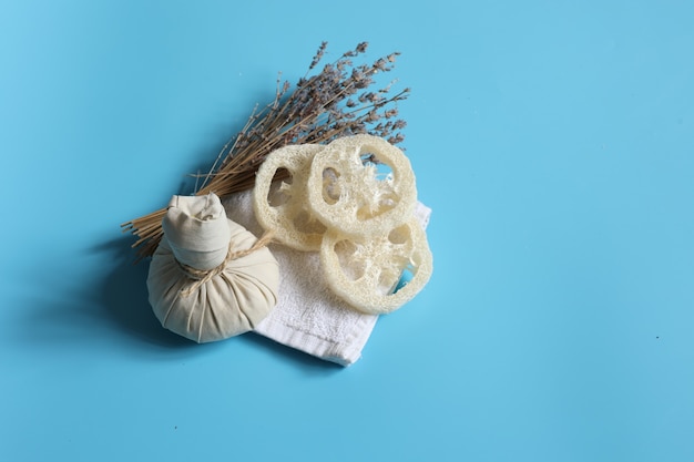 Spa-Komposition mit Kräuterbeutel, Luffa und Lavendel auf blauem Hintergrund.