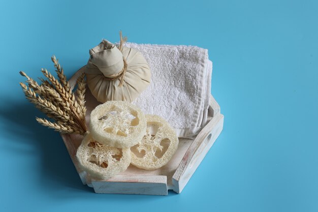 Spa-Komposition mit Kräutermassagebeutel, Luffa, Handtuch und Weizen auf blauem Hintergrund, Kopierraum.