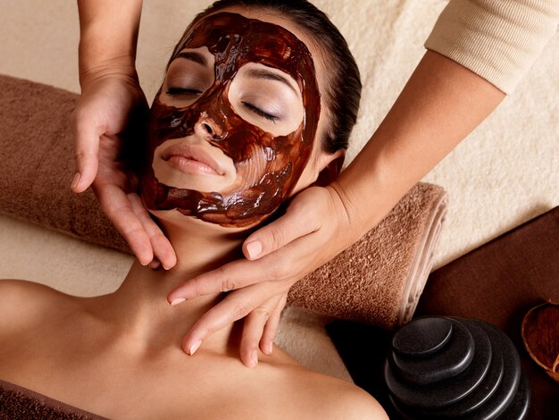 Spa-Massage für junge Frau mit Gesichtsmaske im Gesicht - drinnen