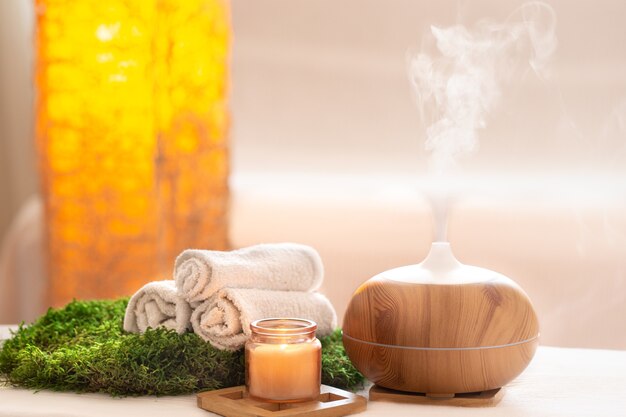 Spa-Zusammensetzung mit dem Aroma eines modernen Öldiffusors mit Körperpflegeprodukten. Gedrehte weiße Handtücher, Frühlingsgrün und Blumen. Spa-Konzept für Körper und Gesundheit.