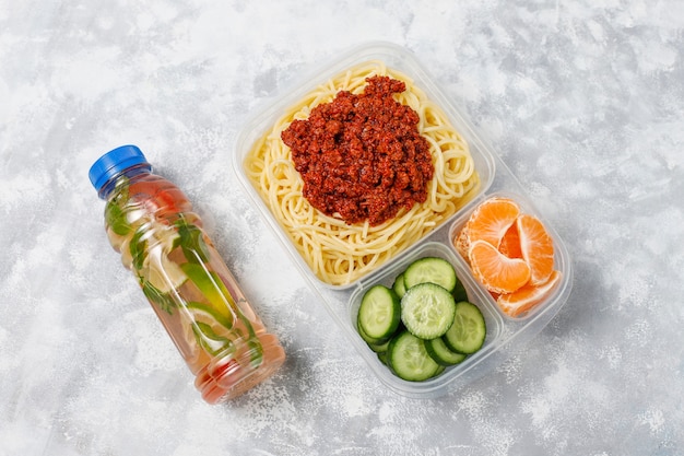 Spaghetti Bolognese zum Mitnehmen in einer Plastikbrotdose mit Detoxgetränk und Fruchtscheibe auf Licht