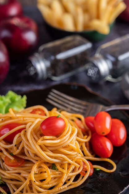 Spaghetti in einer schwarzen Tasse mit Tomaten und Salat.