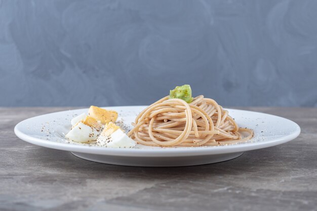 Spaghetti mit gekochtem Ei auf weißem Teller.