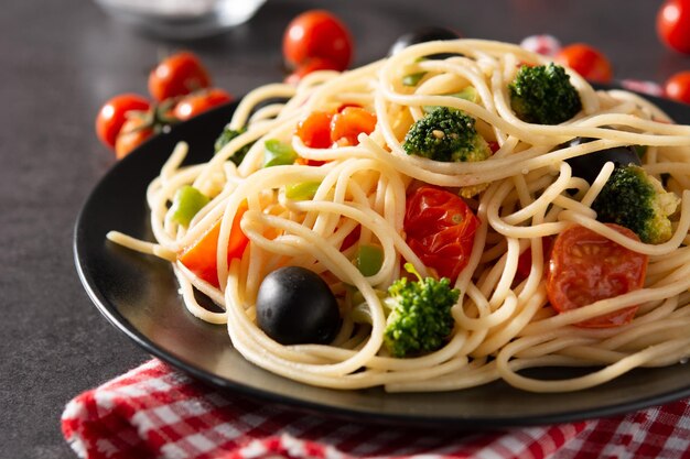 Spaghetti mit Gemüsebroccolitomatoespeppers auf schwarzem Schieferhintergrund