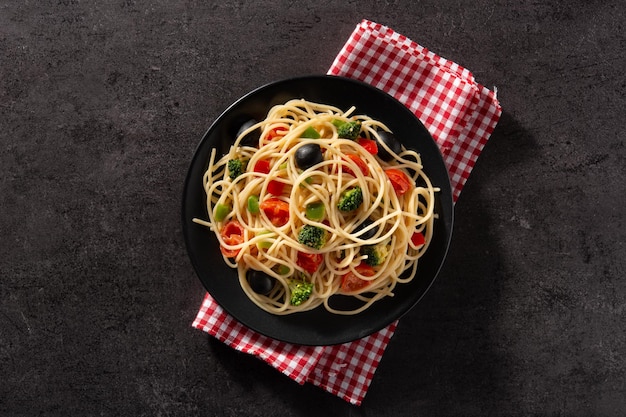 Spaghetti mit gemüsebrokkolitomatenpaprika auf schwarzem hintergrund