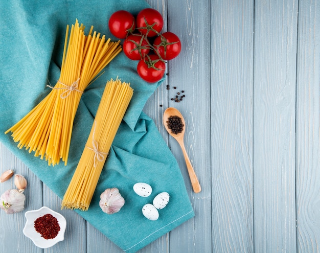 Spaghetti und Linguini auf blauem Hintergrund Pfeffer Tomaten Knoblauch Knoblauch Eier Draufsicht Kopienraum