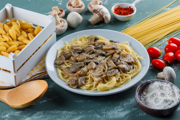 Spaghetti und Pilze mit rohen Nudeln, Tomaten, Mehl, Gewürzen, Holzlöffel in einem Teller