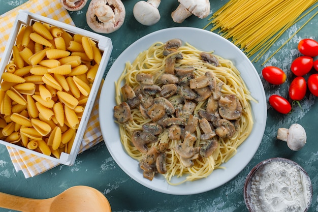 Spaghetti und Pilze mit rohen Nudeln, Tomaten, Mehl, Holzlöffel in einem Teller auf Gips