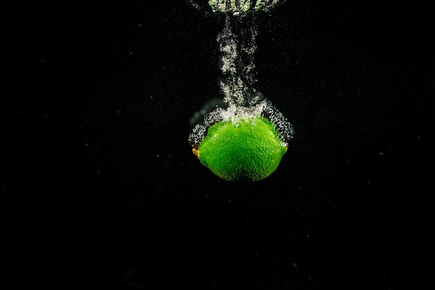 Sparkling green lime spritzt Wasser auf schwarzem Hintergrund