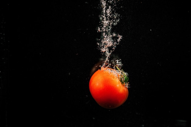 Sparkling rote Tomate fällt in Wasser und spritzt es