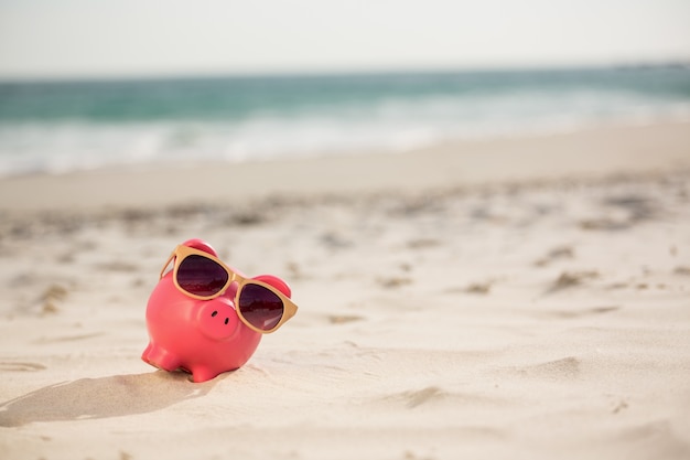 Sparschwein mit Sonnenbrille gehalten auf Sand