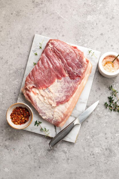 Speck und Zutaten für die Herstellung von hausgemachter Porchetta Ein traditionelles italienisches Gericht für die Feiertage auf grauem Betonhintergrund
