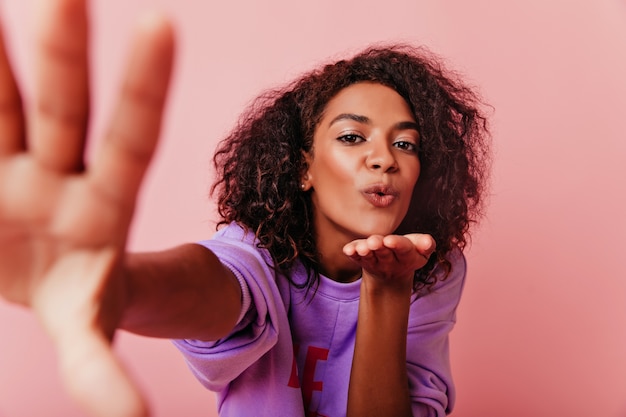 Spektakuläre afrikanische Frau, die Liebe ausdrückt, während sie selfie macht. Optimistisches lockiges Mädchen, das Foto von sich selbst macht.