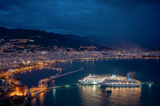 Spektakuläre Nacht an der Seeküste mit Lichtern der Stadt und des Kreuzfahrtschiffs, die sich im Wasser spiegeln
