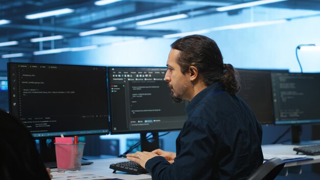 Spezialist am PC-Schreibtisch in einer Hightech-Einrichtung, der die Serverreihen beaufsichtigt