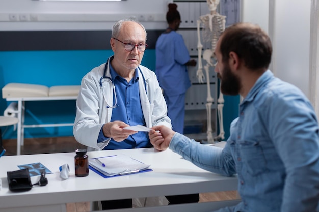 Spezialist, der einem kranken Patienten beim Kontrollbesuch Rezeptpapier aushändigt